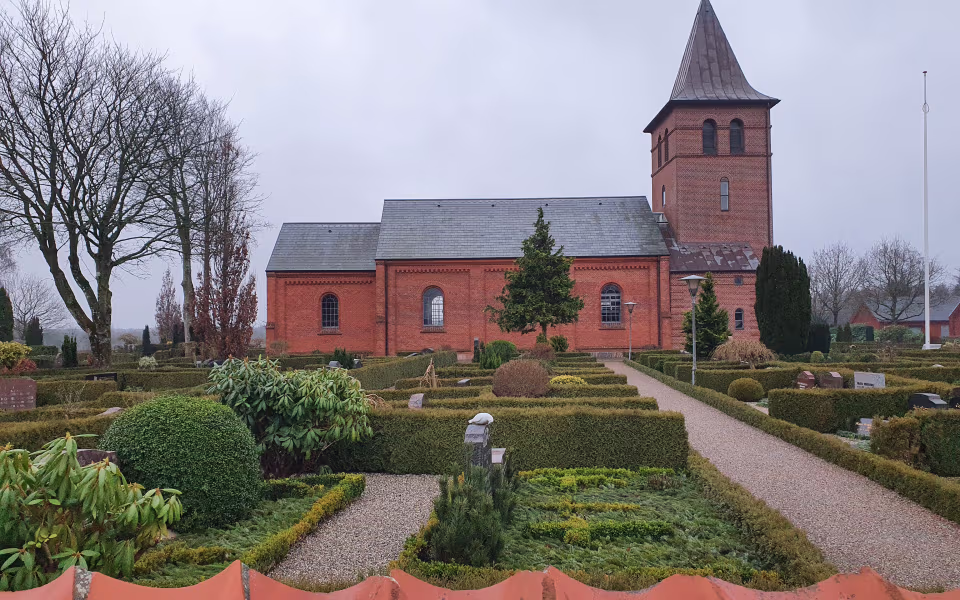 Kirkegård med hække foran Grene Kirkes røde murstenstårn