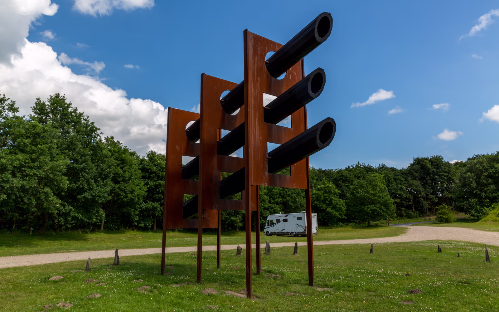 Rustfarvet skulptur med sorte rør i Tørskind Grusgrav ved grussti og skov