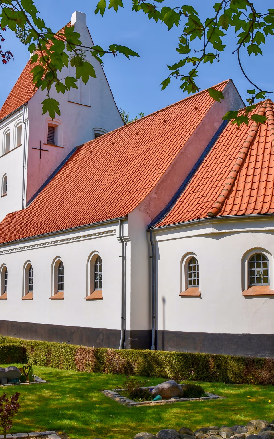 Urup Kirke med rødt tegltag og kirkegård under grønne og røde trækroner