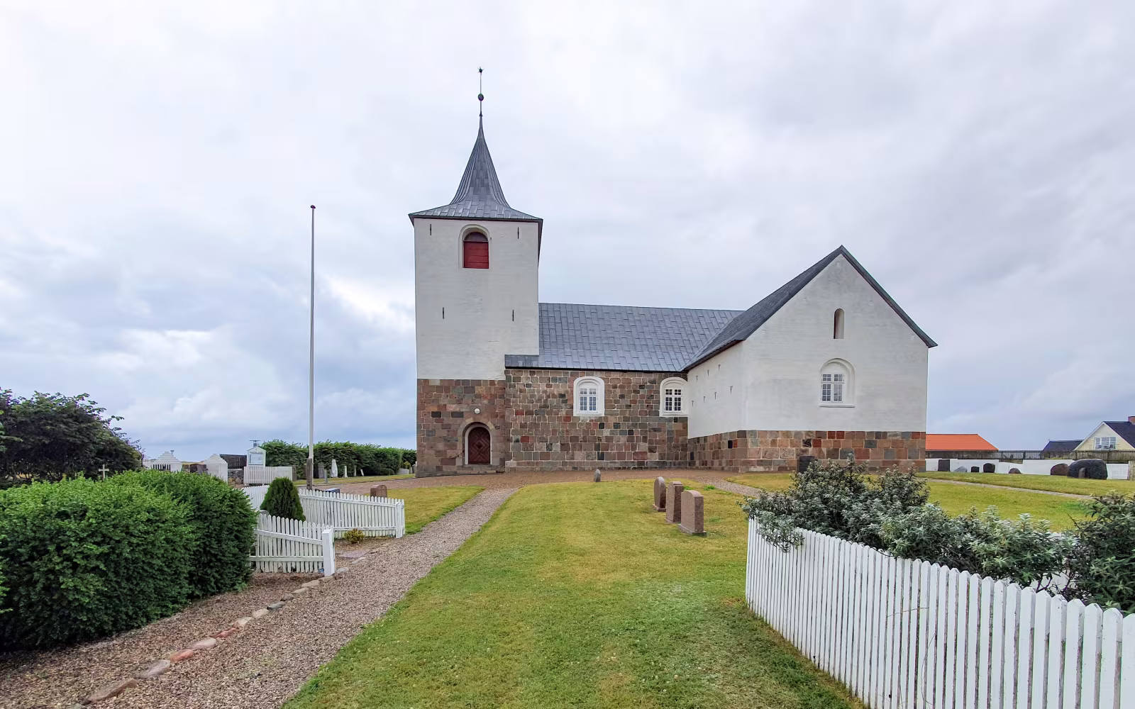Fjaltring Kirke med hvidt tårn, kirkegård og grussti foran