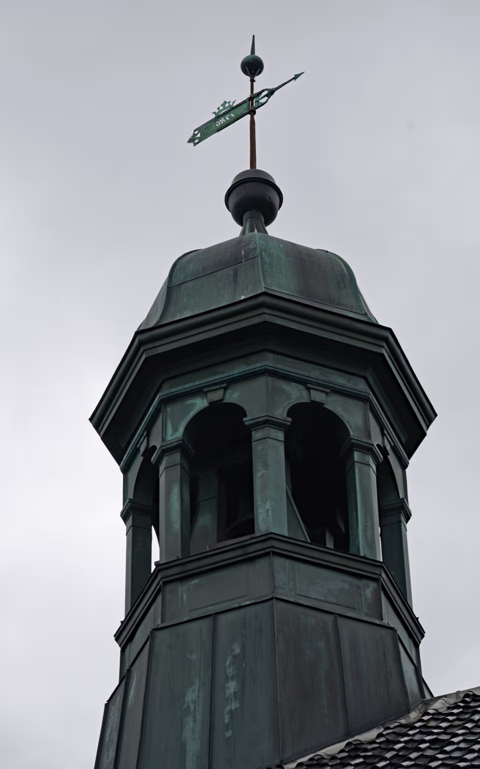 Vindfløj på kobbertaget af Nordby Kirke på Fanø mod grå himmel