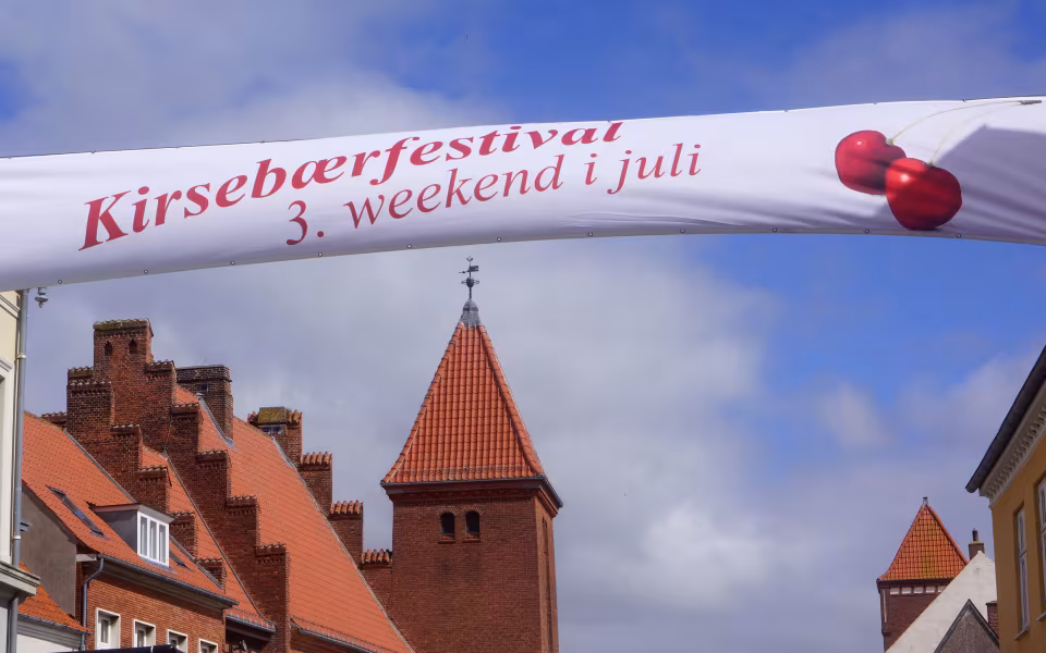 Banner for kirsebærfestival i Kerteminde over røde tegltage og kirketårn