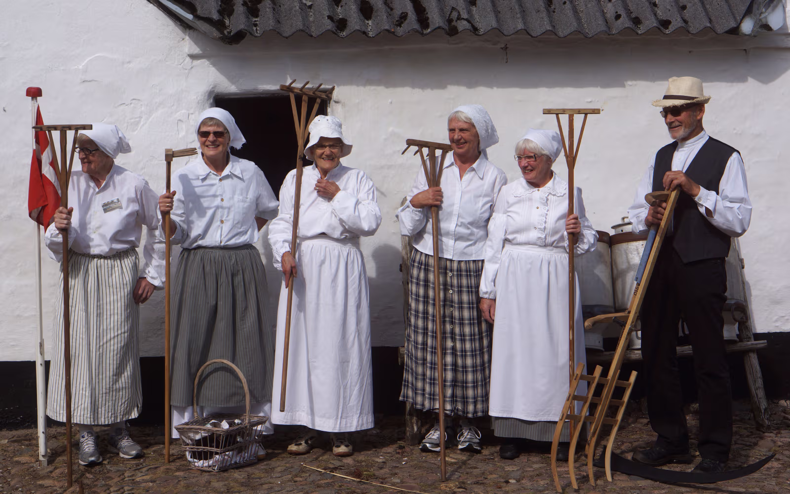 Folk i historiske dragter holder redskaber ved Høstdag på Karensminde
