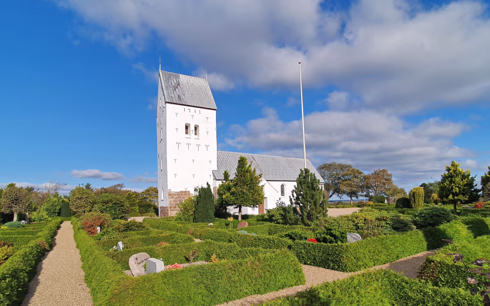 Kirkegårdssti og hvidt kirketårn ved Lønborg Kirke under blå himmel
