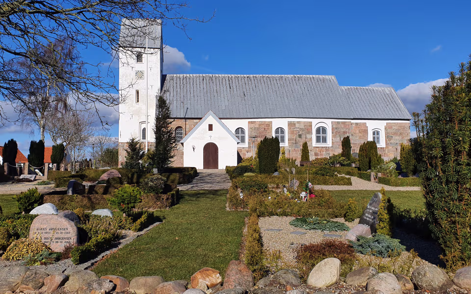 Lunde Kirke med hvidt tårn og kirkegård i forgrunden