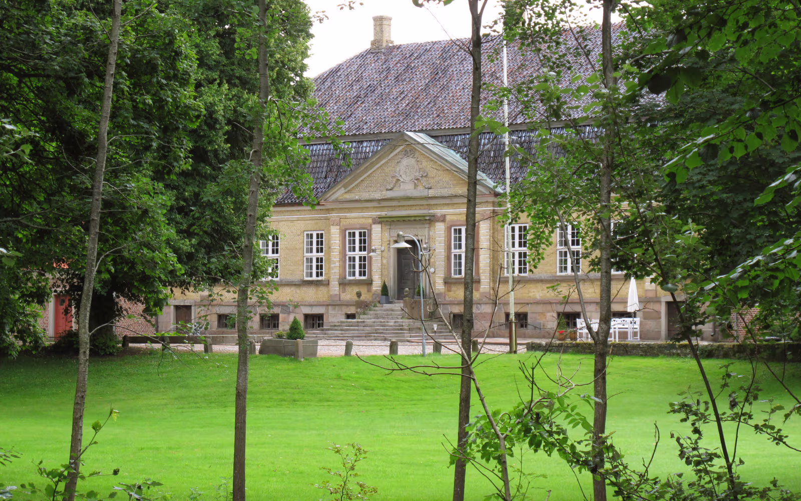 Hovedbygning på Nørholm Gods set gennem grønne træer ved plænen