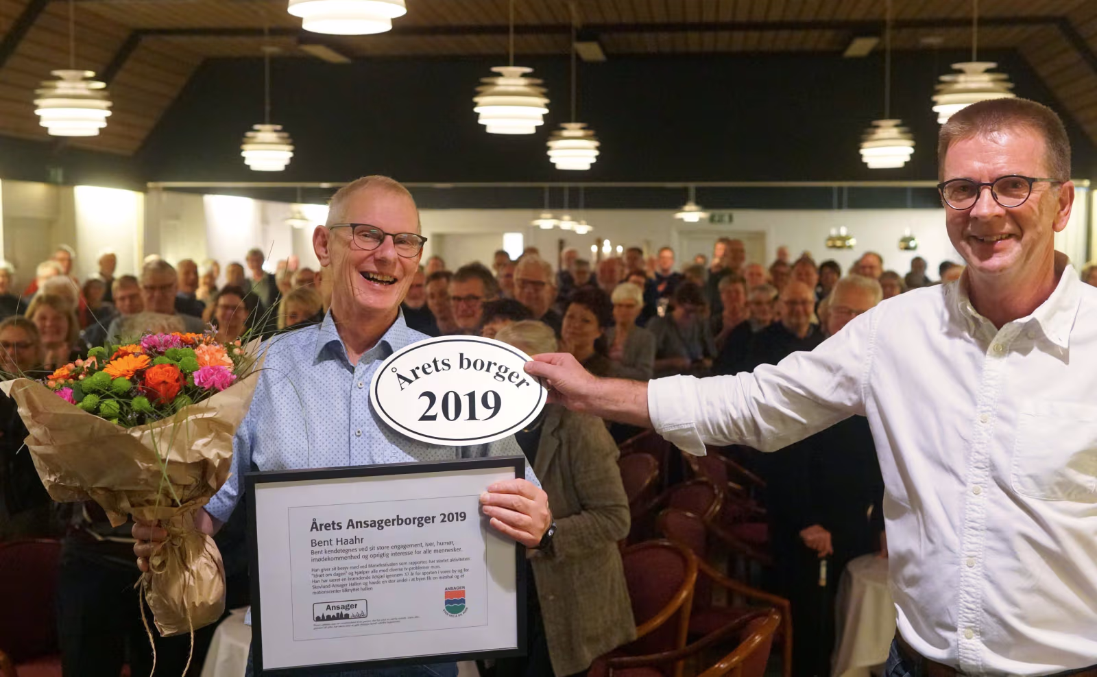 Bent Haahr blev årets Ansagerborger 2019. Finn Grundahl fra Ansager Udviklingsråd overrækker diplom og blomster.