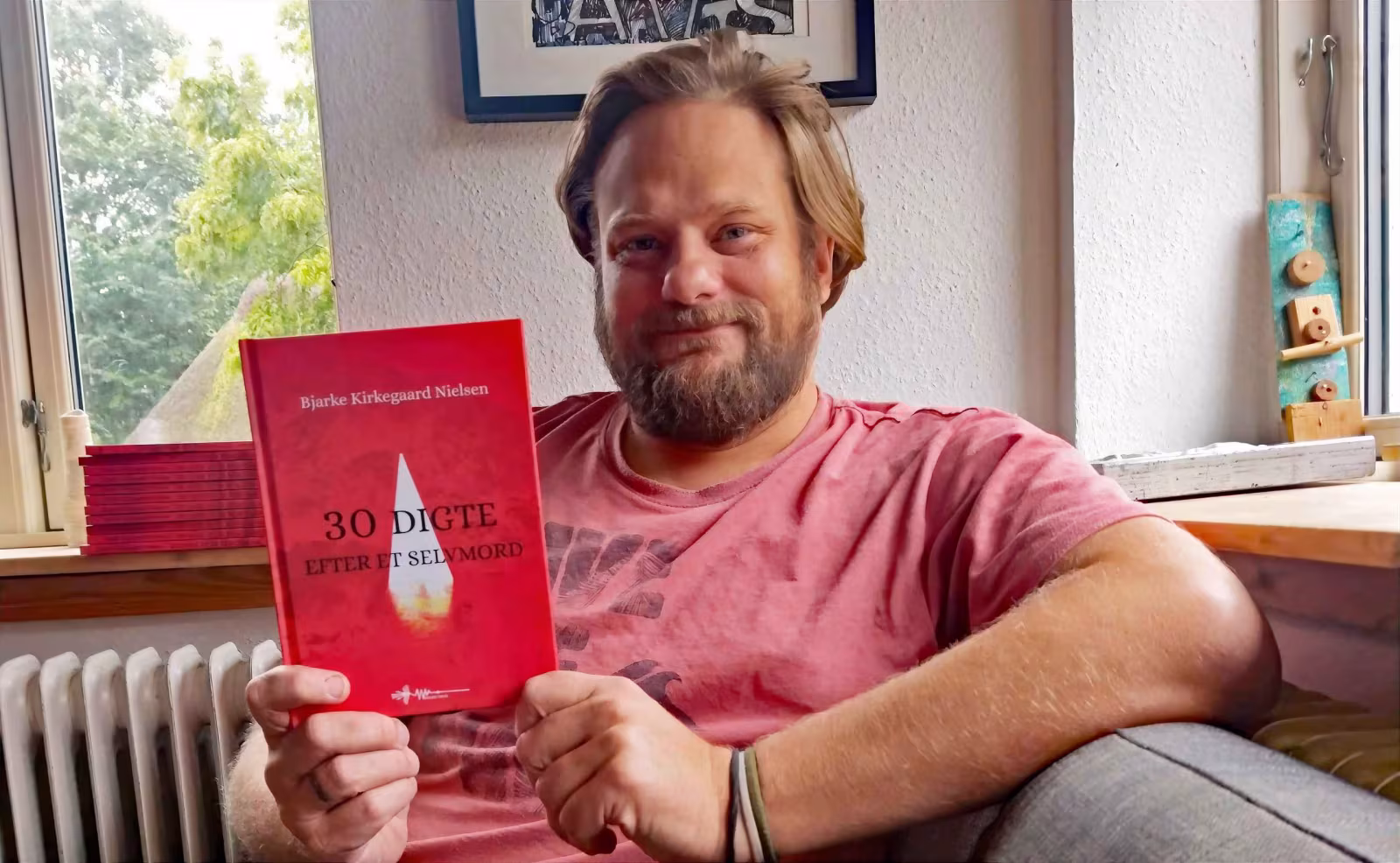 Bjarke Kirkegaard Nielsen sidder med sin nye digtsamling "30 digte efter et selvmord". Bogen indeholder dybt personlige tekster skrevet efter en tragisk familiebegivenhed og har allerede ramt mange læsere.