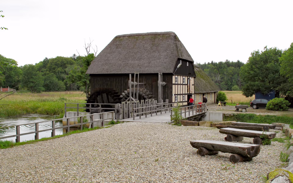 Stråtækt vandmølle ved Nørholm Vandmølle med træbroer over roligt vand
