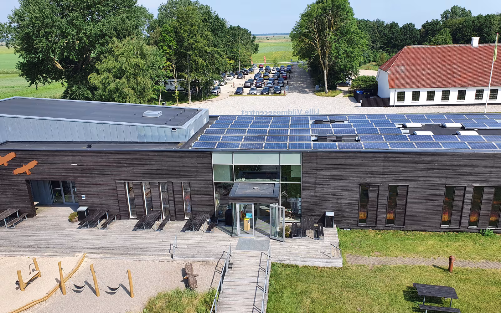 Solcellepaneler på taget af Lille Vildmosecentret med legeplads og skov bagved