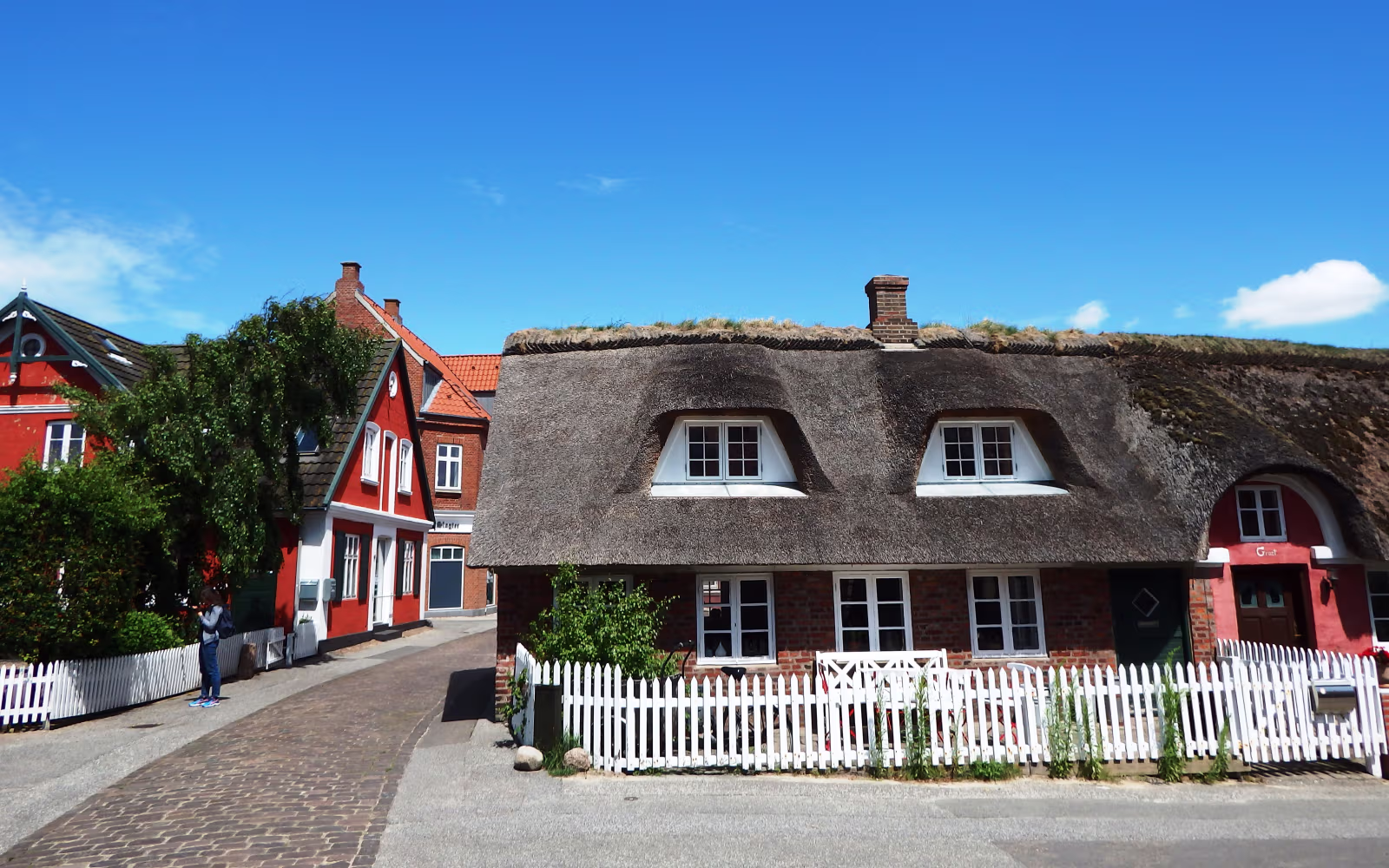 Stråtækte huse og hvide stakitter langs brostensvej på Fanø