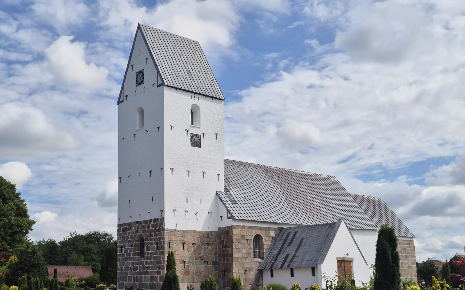 Ølgod Kirke med hvidt tårn og grøn kirkegård under skyet himmel