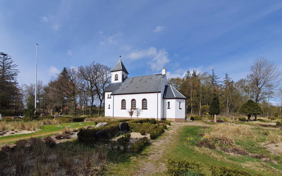 Børsmose Kirke ved kirkegård med gravsten, flagstang og blå himmel