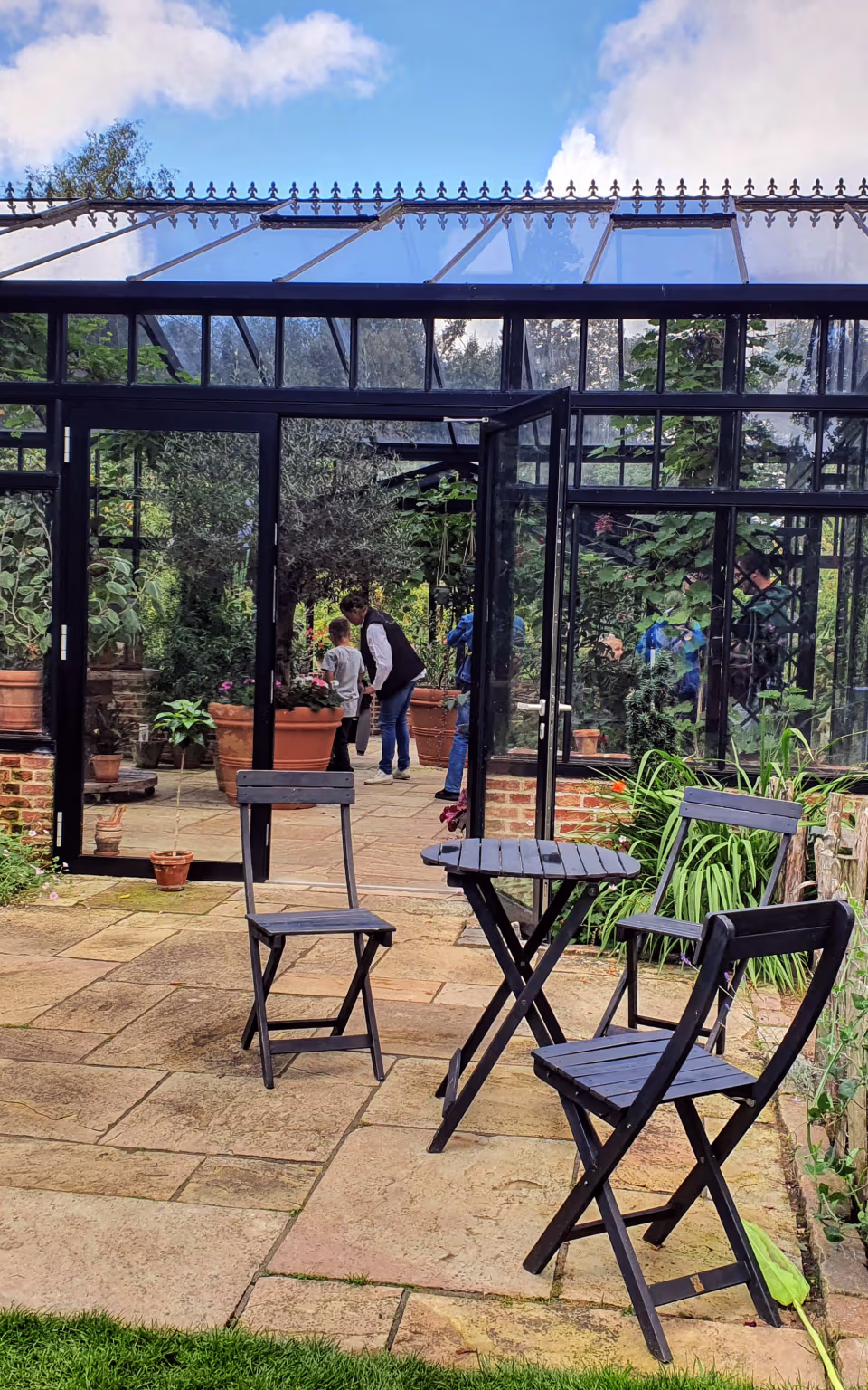 Drivhus ved Tambours Have omgivet af blomster, terrasse og sorte caféstole