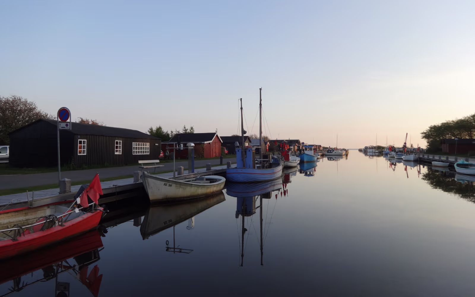 Både ligger spejlblankt i Stauning Havn foran røde og sorte havnehuse