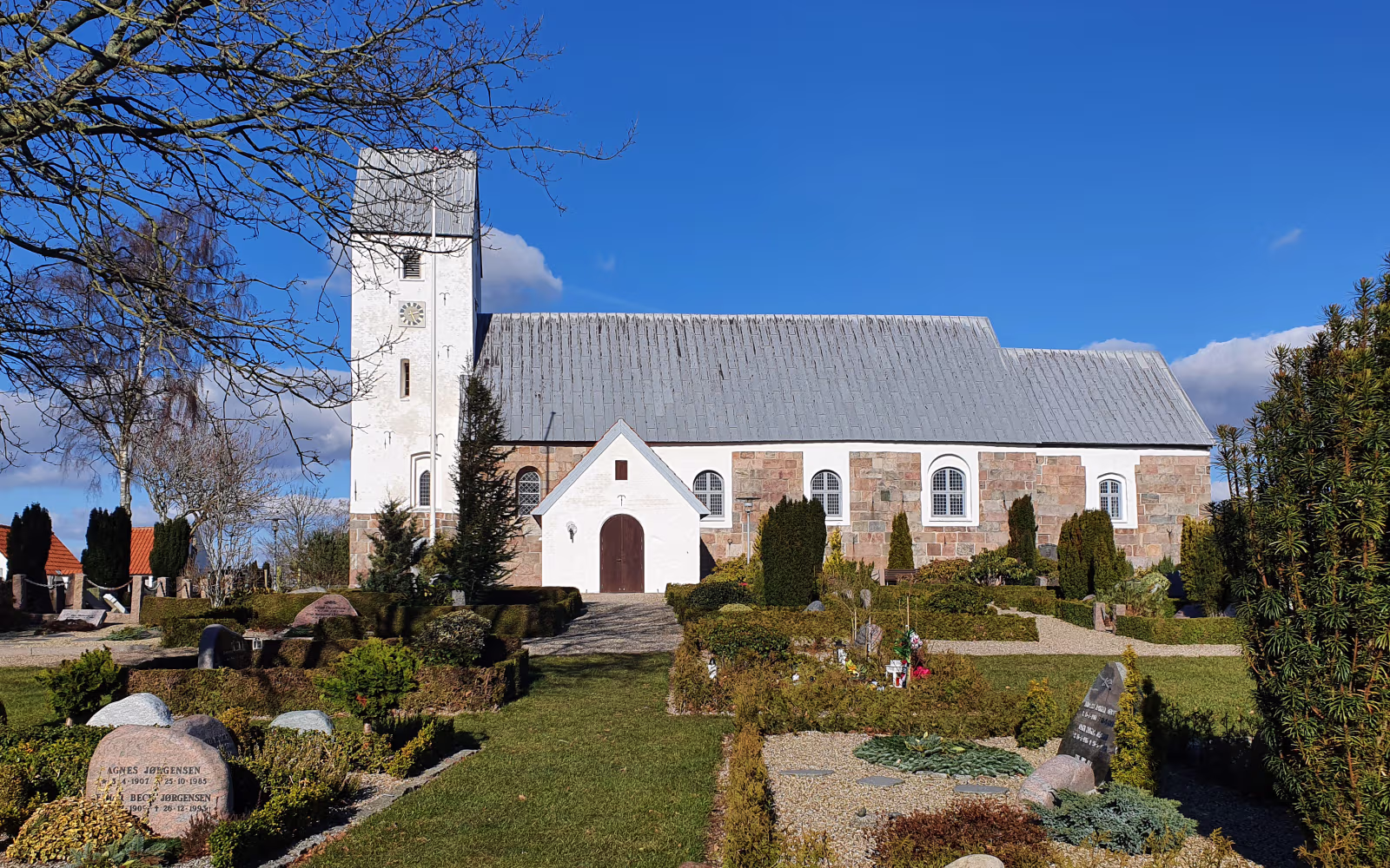 Lunde Kirke med hvidt tårn og kirkegård i forgrunden