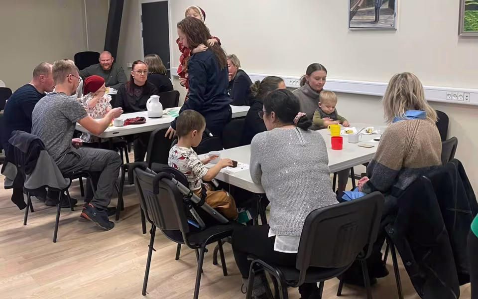 Børn og dagplejere samles omkring bordet, iført nissehuer, for at nyde et hyggeligt måltid sammen. Et øjeblik af fællesskab og julestemning