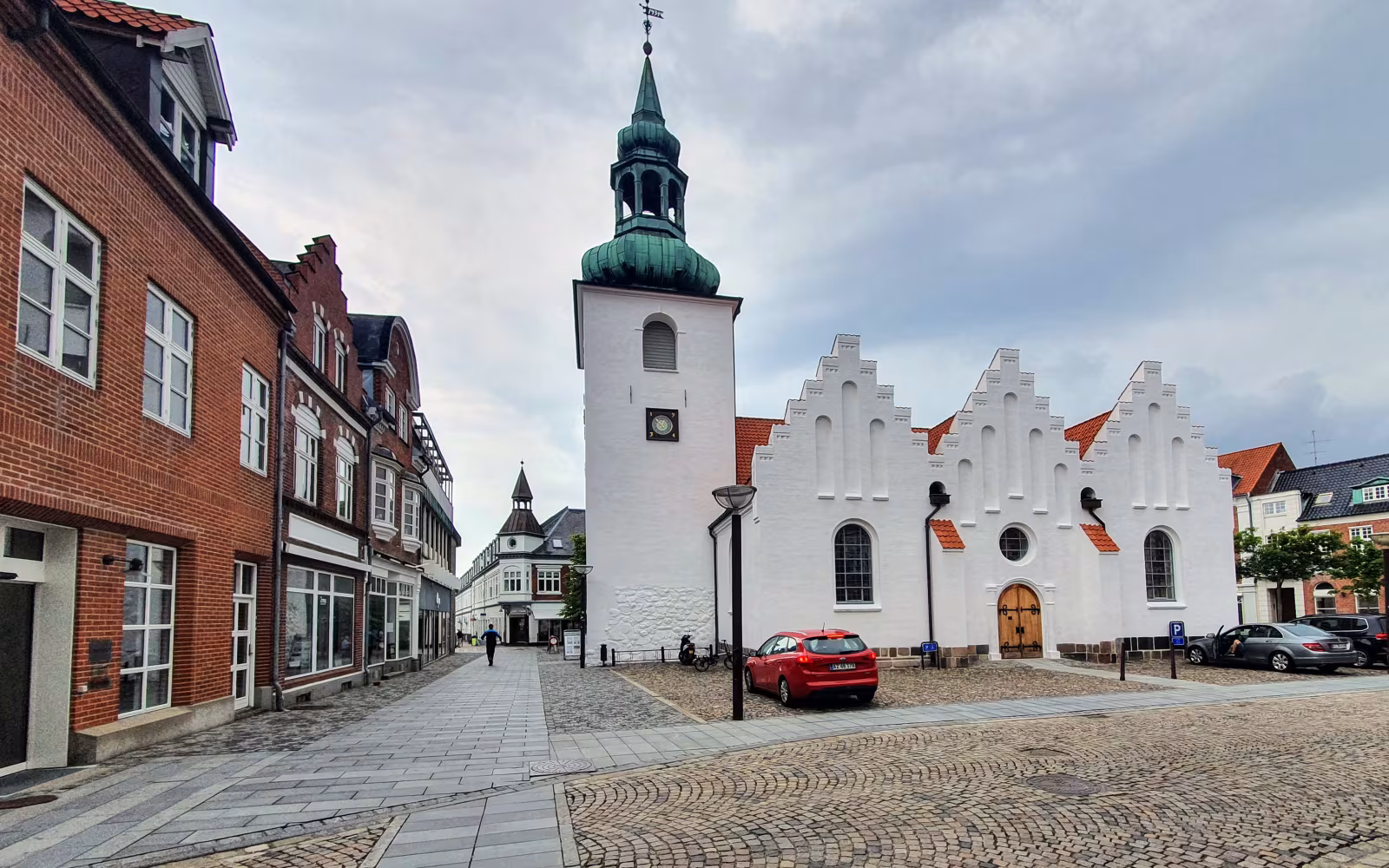 Lemvig Kirkes hvide tårn ved brostensbelagt gade med røde murstenshuse