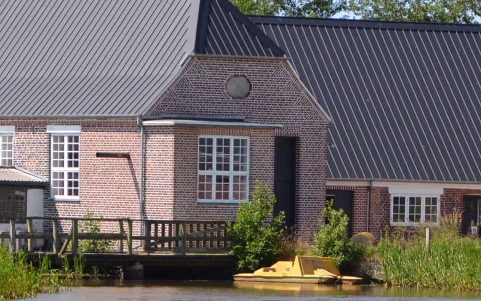 Lydum Mølle med træbro over vandet og gul båd ved bredden