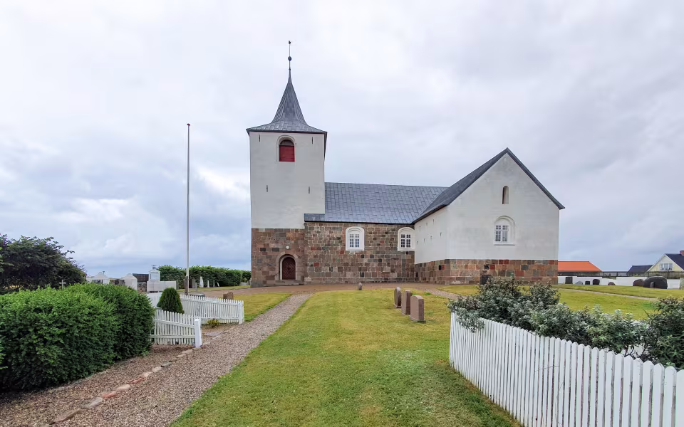 Fjaltring Kirke med hvidt tårn, kirkegård og grussti foran