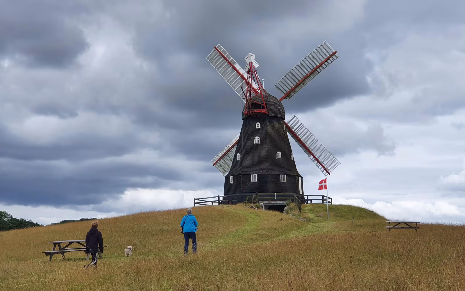 Vindmølle ved Skovsgaard Mølle med besøgende i græsset under mørke skyer