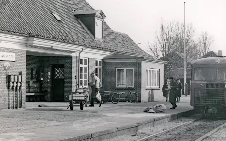 Foto fra togudstillingen: Persontoget fra Grindsted er netop ankommet til Ansager Station, hvor post og pakker bliver fordelt. I forgrunden ses Hans S. Nissen, kaldet “Pakhans”, som kom cyklende fra byen på sin gamle budcykel. Han kørte gennem mange år rundt med pakker i Ansager – først med hestevogn, senere på cykel
