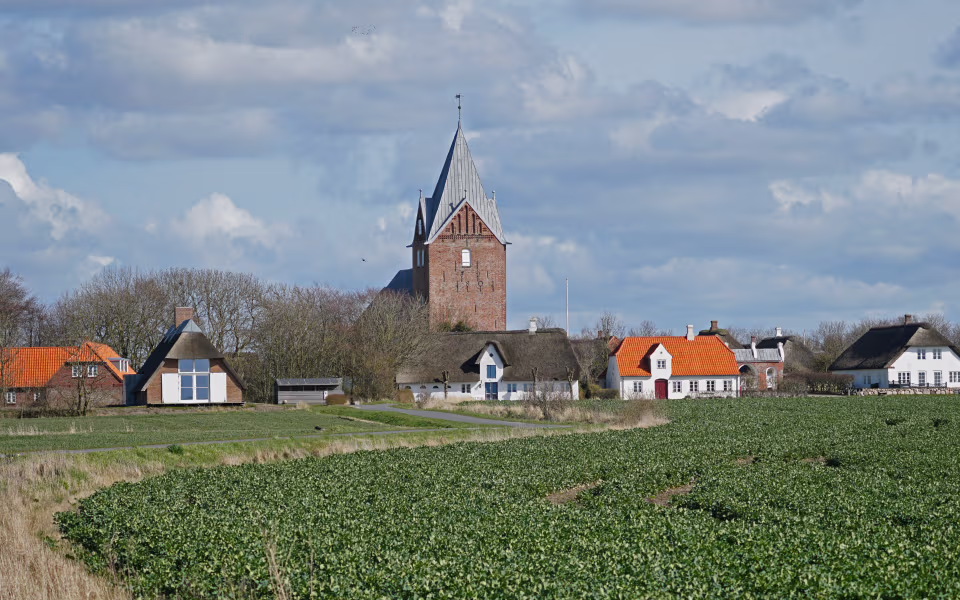 Ballum Kirkes tårn over landsbyhuse og grønne marker under skyet himmel