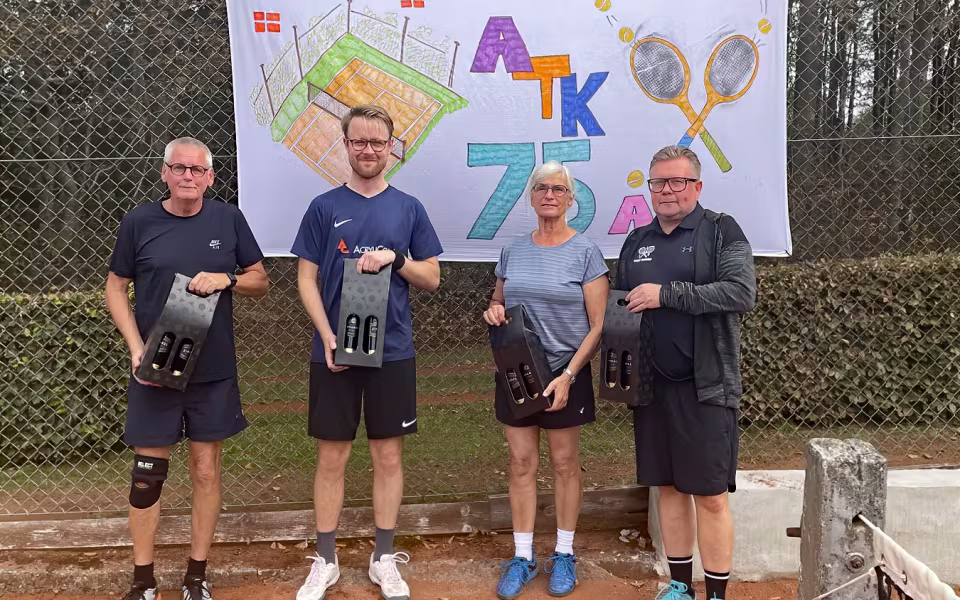 Glade Ansager Tennis Klub medlemmer samlet ved bordene foran klubhuset, midt i den årlige klubturnering. 75-års jubilæumsfesten venter senere på dagen. Tak til alle for en uforglemmelig dag!