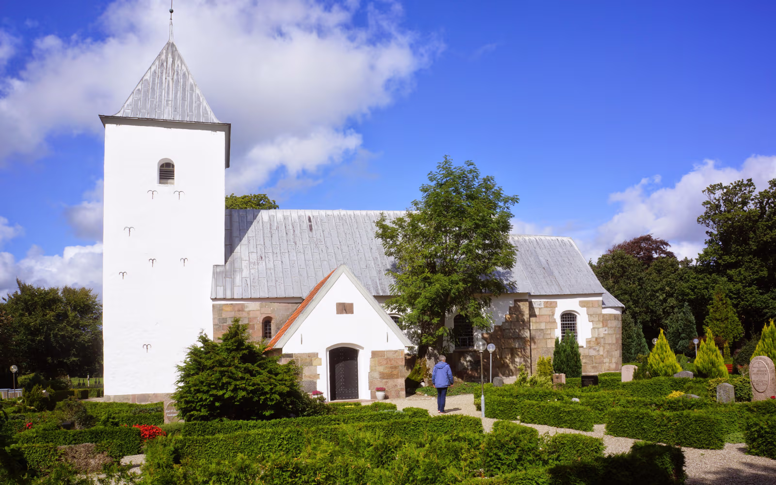 Hvidt kirketårn ved Thorstrup Kirke med kirkegård og grønne hække foran