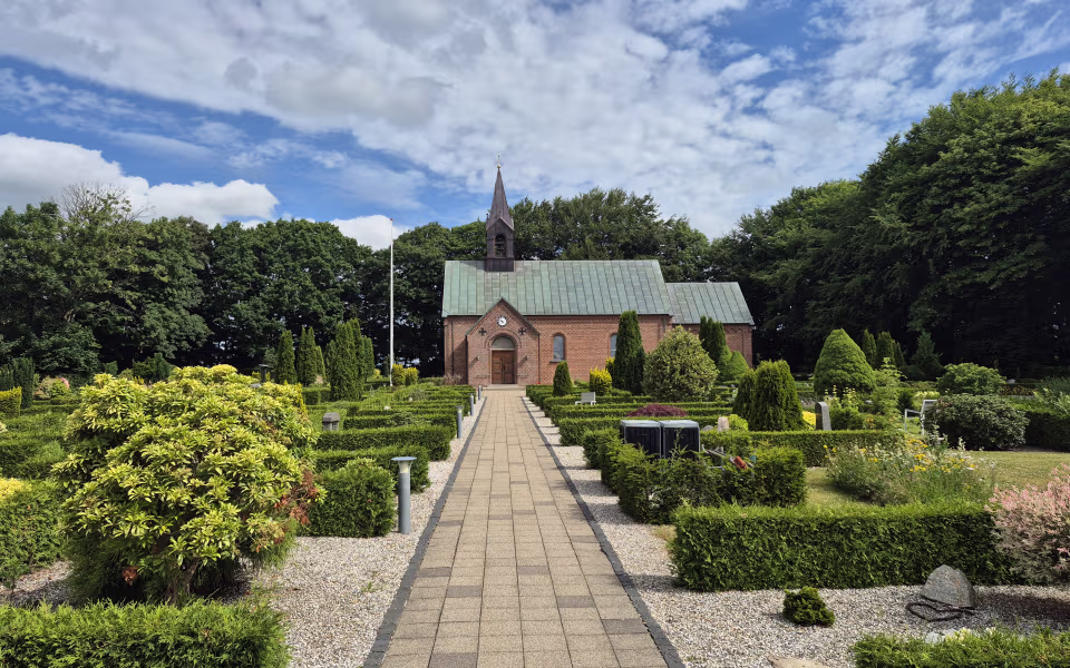 Flisegang gennem kirkegården op til Bejsnap Kirke under skyet sommerhimmel