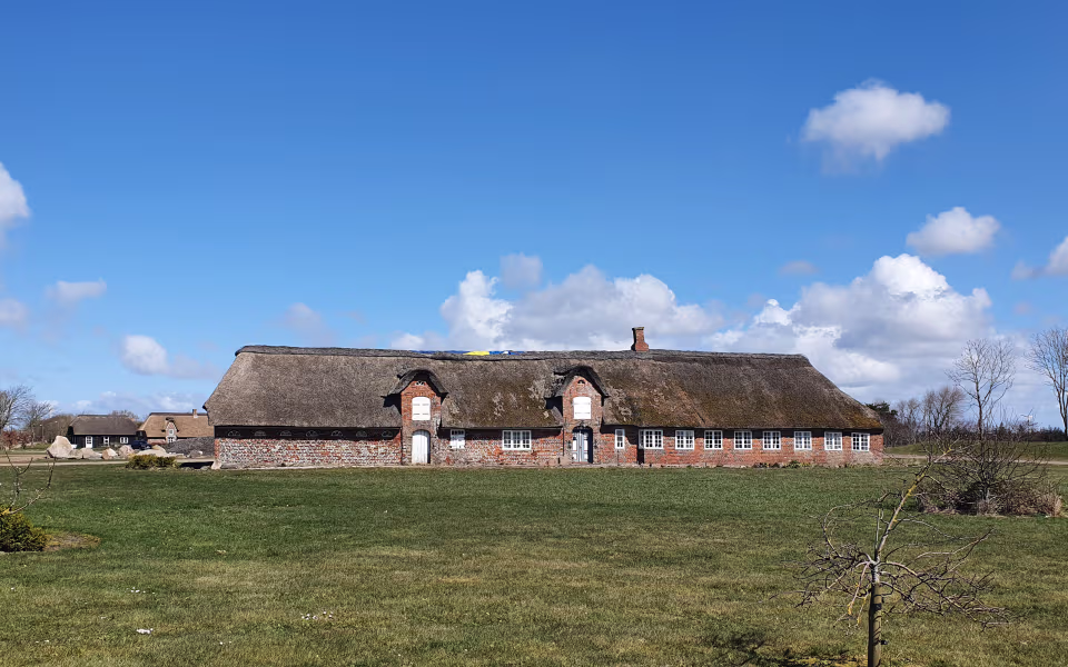 Stråtækt murstenshus i Hjerpsted By under blå himmel med skyer