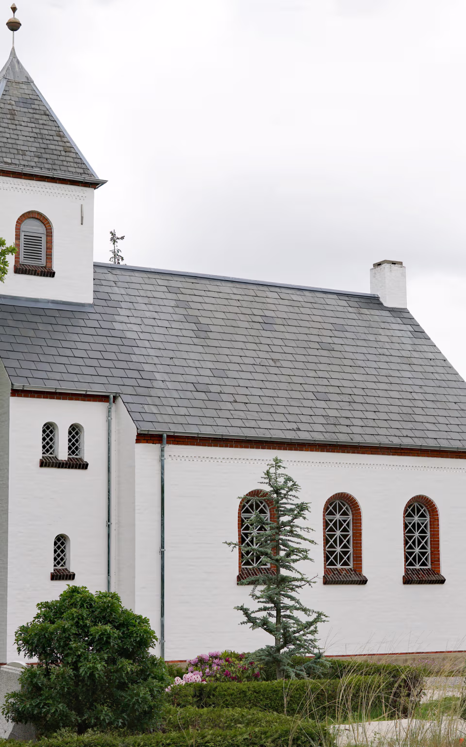 Børsmose Kirke med hvidt tårn, skifertag og grønne træer omkring kirkegården