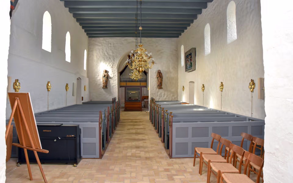 Kirkeskib i Billum Kirke med grå bænke, orgel og gylden lysekrone