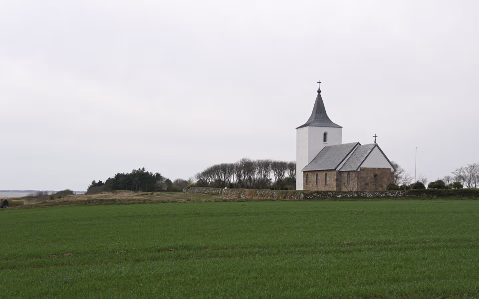 Gammelsogns Kirke med hvidt tårn ved grøn mark og kyst