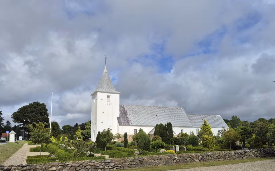 Aal Kirke med hvidt tårn, gråt tag og kirkegård bag lav kampestensmur