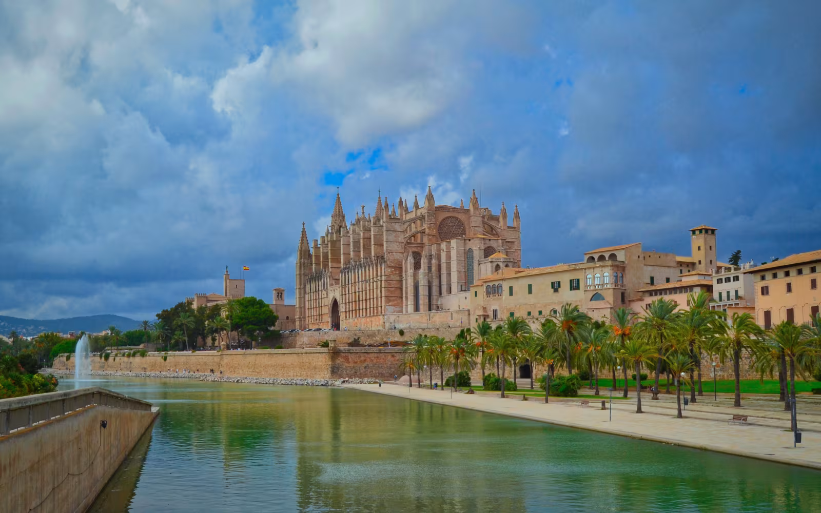 La Seu-katedralen ved vandbassinet med palmer og mørke skyer over Palma
