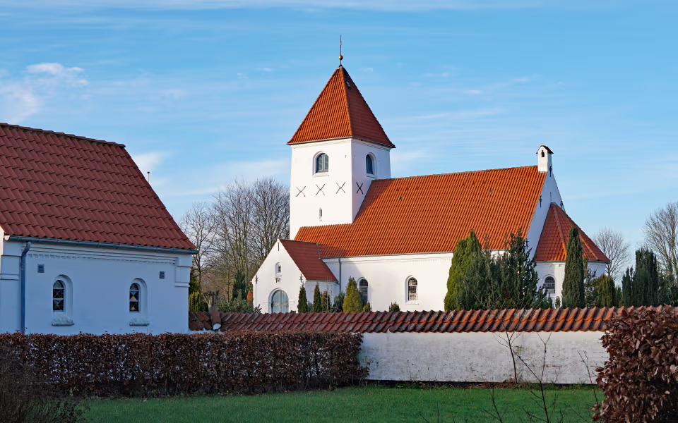 Kirketårn ved Skovlund Kirke mellem røde tegltage og hvide mure