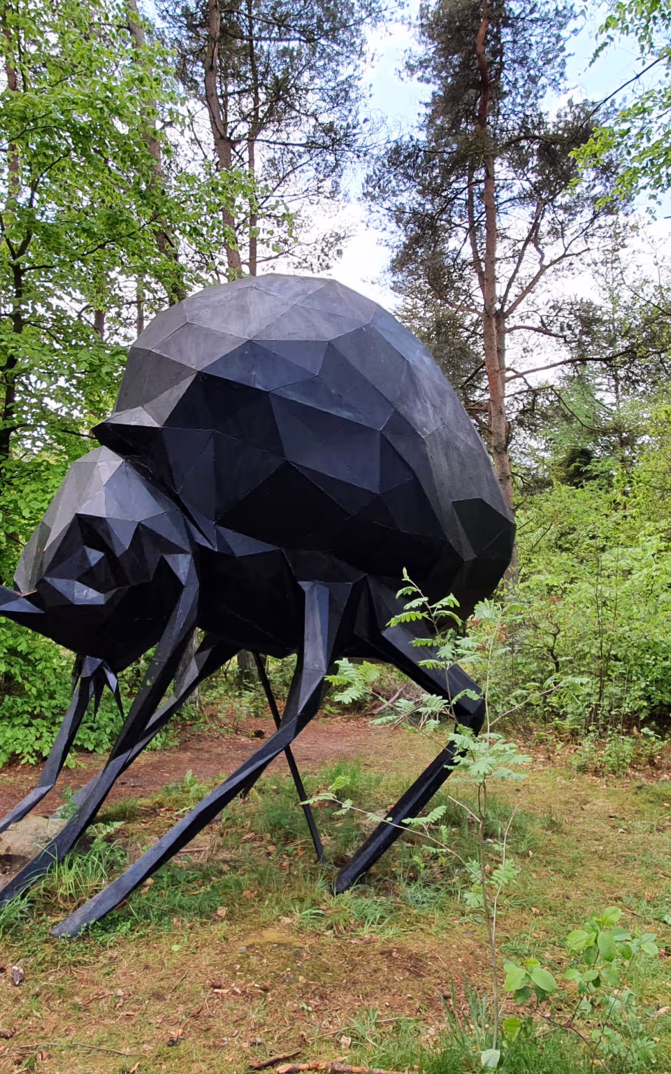 Sort lavpoly-skulptur af kæmpe insekt i grøn skov