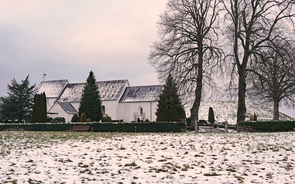 Kirken ved Vikingernes Jelling bag nøgne træer og sneklædt kirkegård