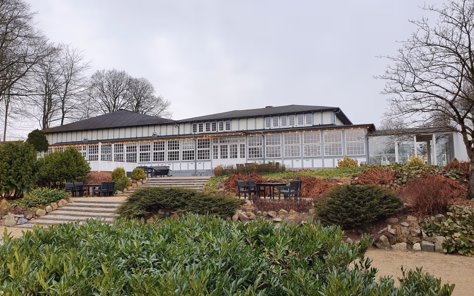 Trappe og have foran hvid bygning med store vinduer i Arnbjergparken