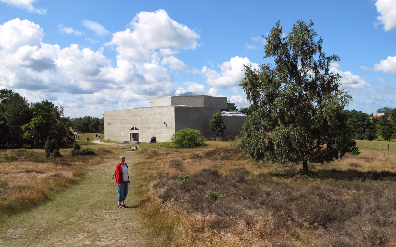 Rudolph Tegners Museum bag lyngklædt sti med besøgende under skyet sommerhimmel