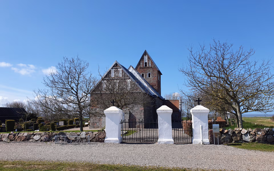 Hjerpsted Kirke bag kirkegårdsmur og bladløse træer under blå himmel