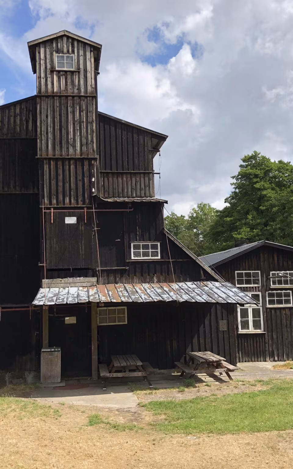 Gammel træbygning ved Klostermølle Papirfabrik med tårn, skure og picnicborde foran