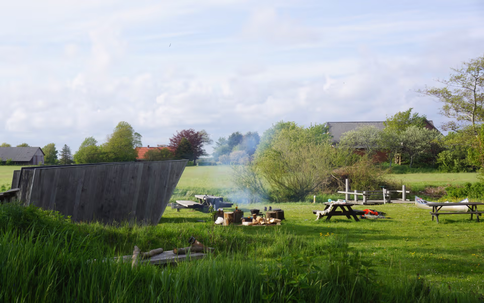 Træshelter ved Kongeåen med picnicborde, kano og røg fra bålplads