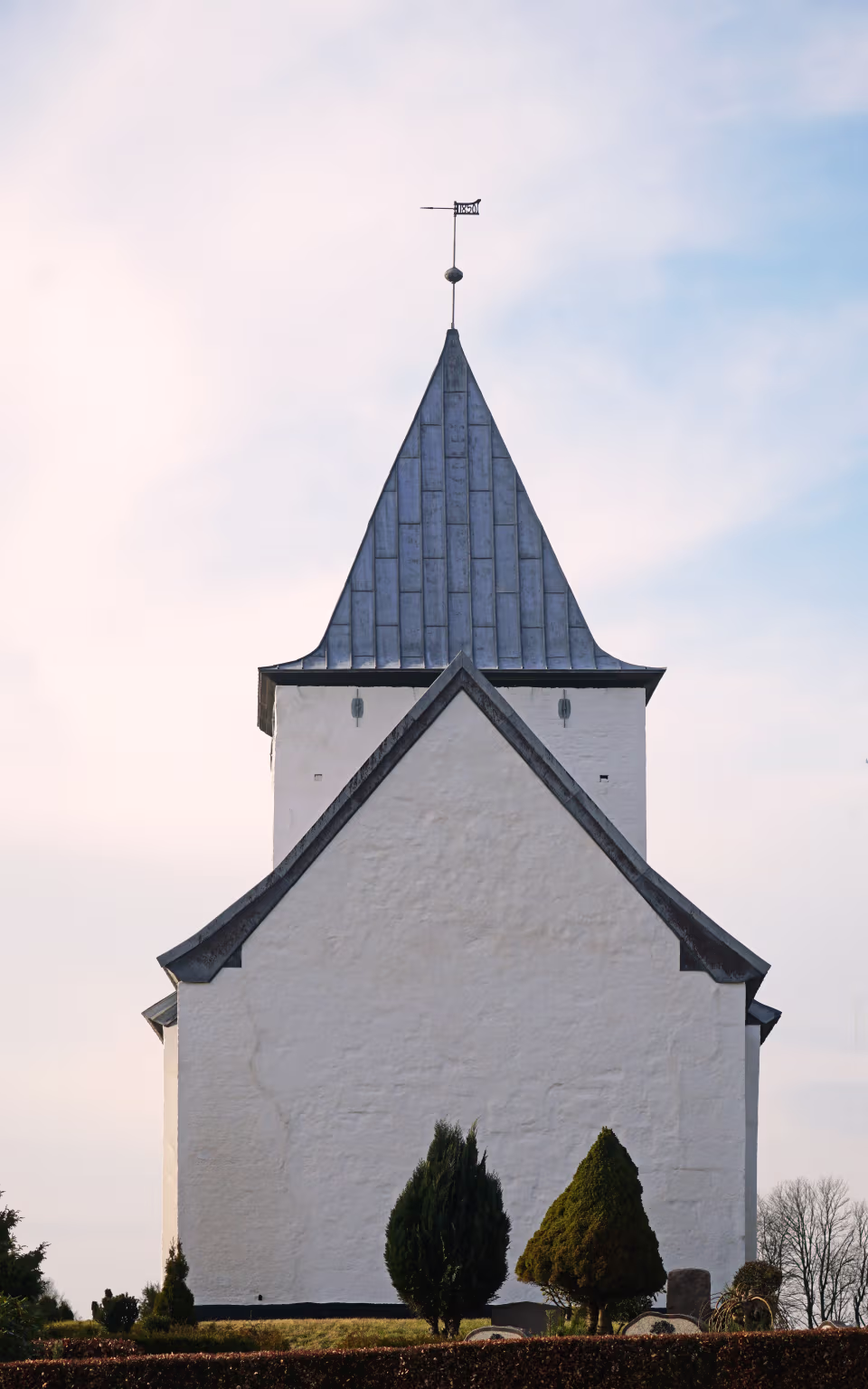 Kirketårn med vejrhane over hvidkalket Starup Kirke og kirkegård