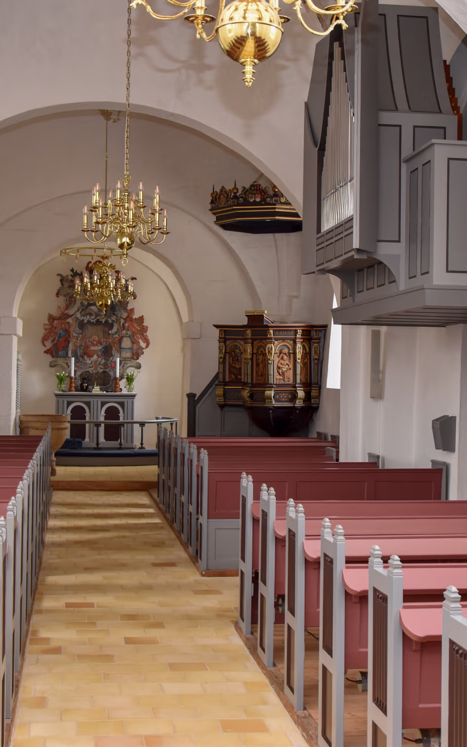 Kirkeskib i Tistrup Kirke med røde bænke, hvælvinger og alter for enden