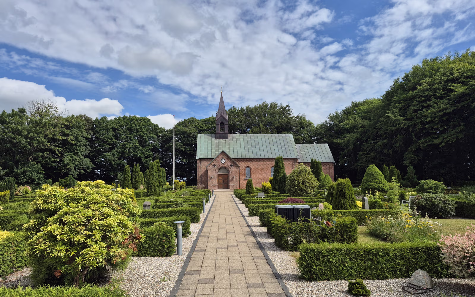 Flisegang gennem kirkegården op til Bejsnap Kirke under skyet sommerhimmel
