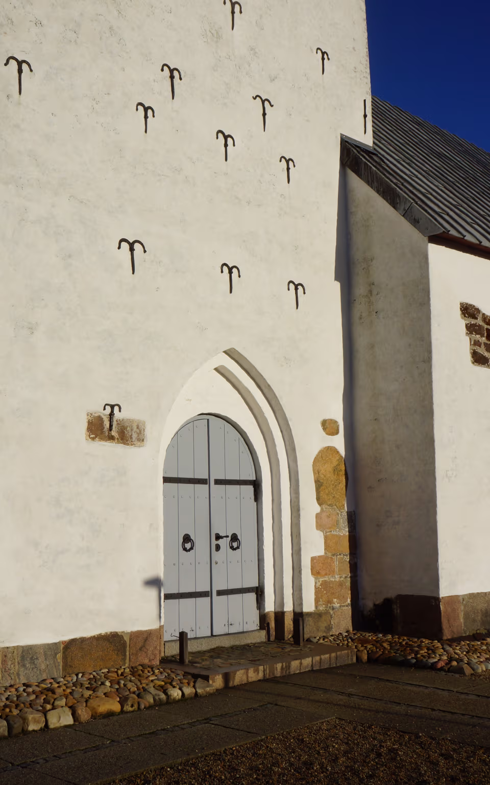Hvidkalket kirke med gråt dørparti og sorte murankre i sollys