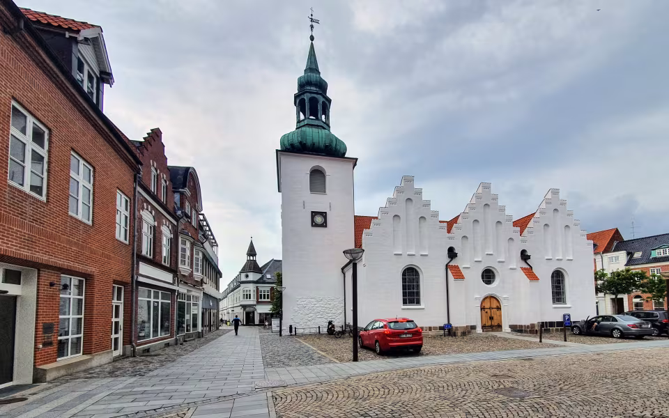 Lemvig Kirkes hvide tårn ved brostensbelagt gade med røde murstenshuse