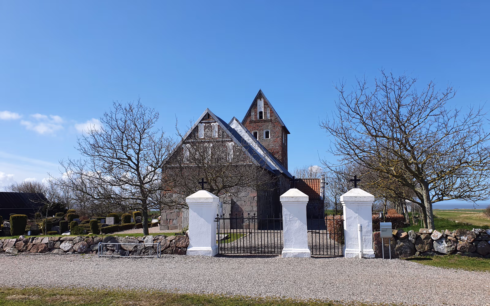 Hjerpsted Kirke bag kirkegårdsmur og bladløse træer under blå himmel